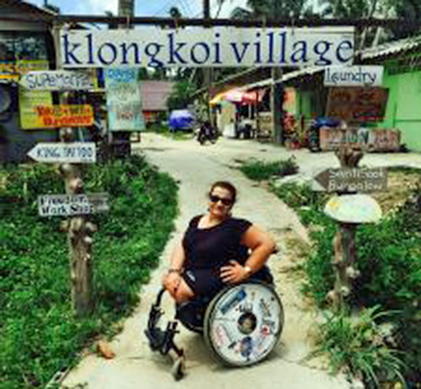 a woman in a wheelchair on a path in front of a sign that says klongkoi village