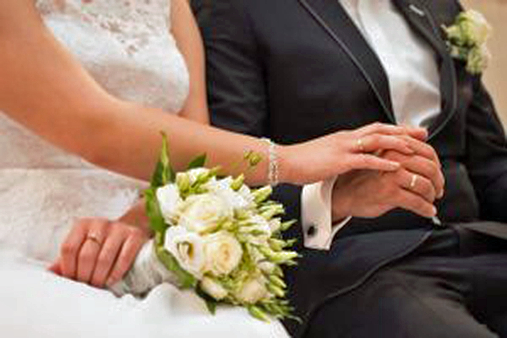 bride and groom are seated, only torsos are visible, holding hands with a bouquet