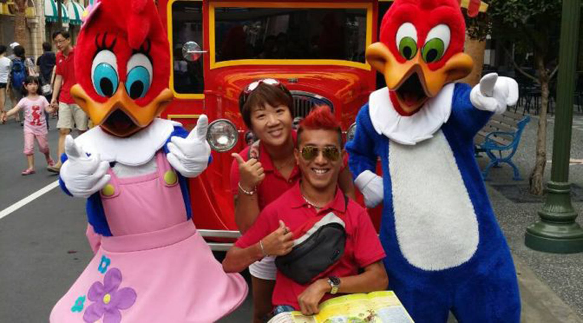 Man in a wheelchair with his girlfriend standing behind, posing with two costumed characters