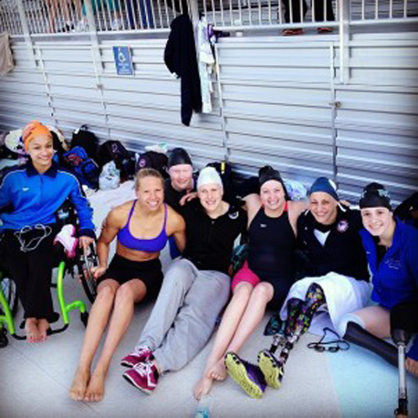 7 athletes on a pool deck, one with a manual wheelchair
