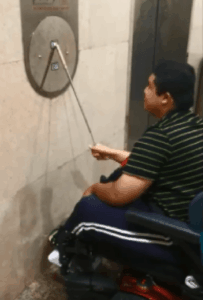 young man in power wheelchair using a device to hit an elevator button