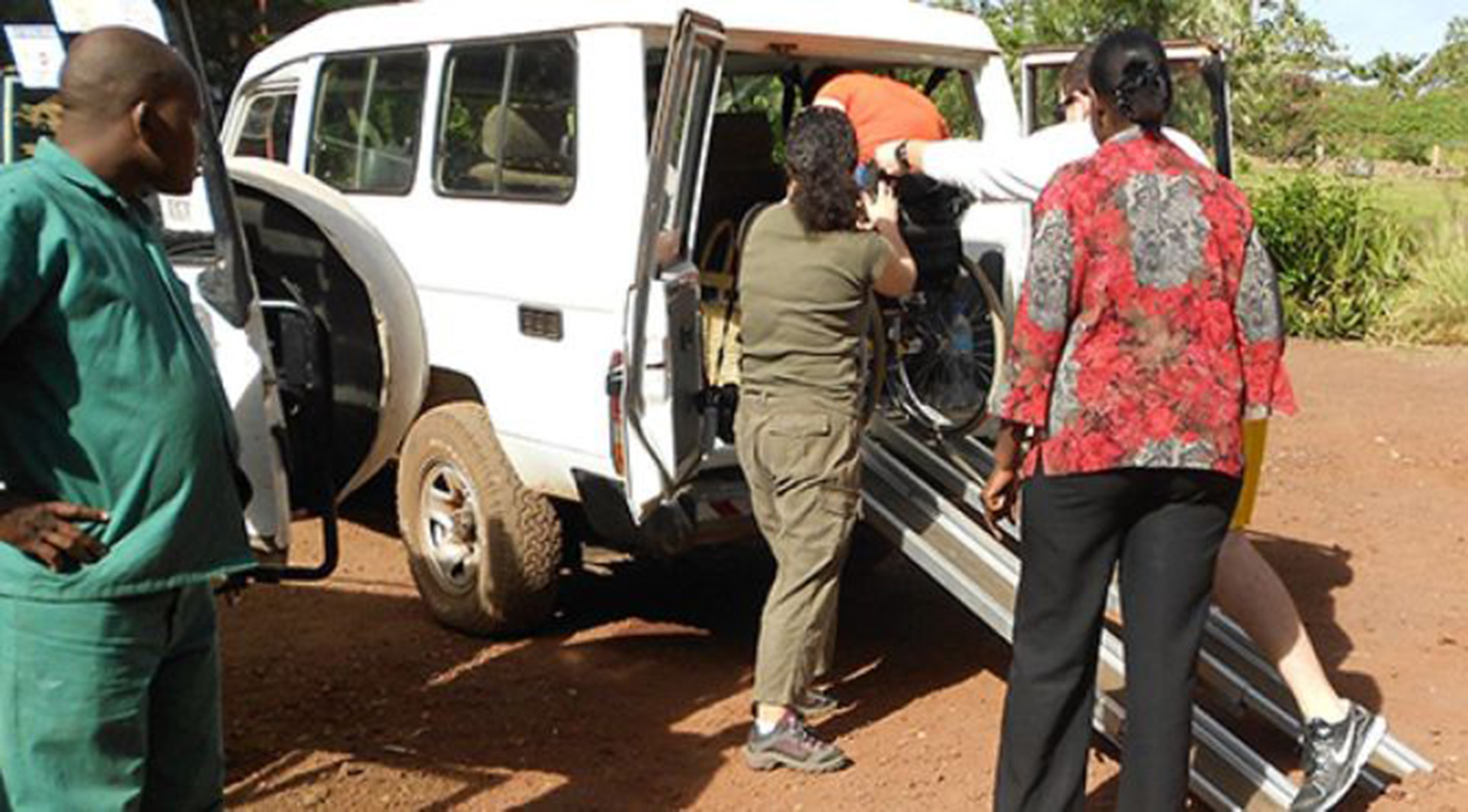 a wheelchair going up a ramp into a van with 3 men standing nearby