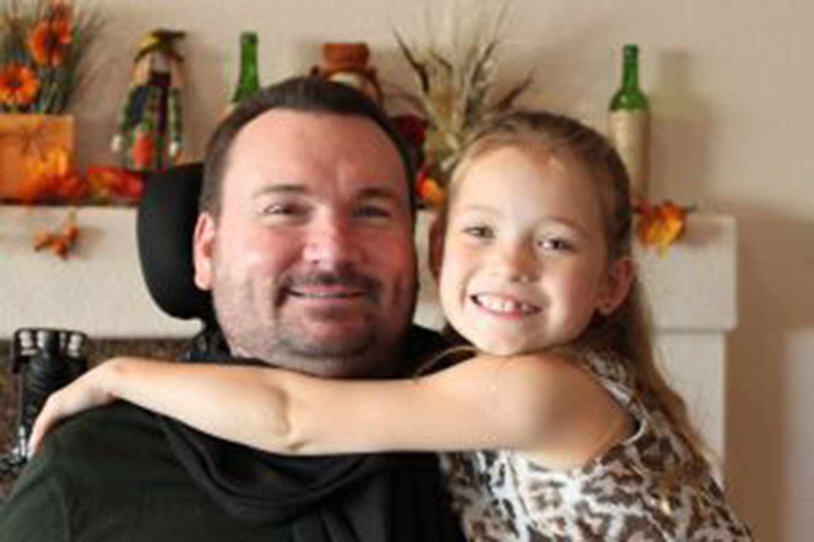 Quadriplegic dad smiling with his young daughter smiling and hugging his shoulders
