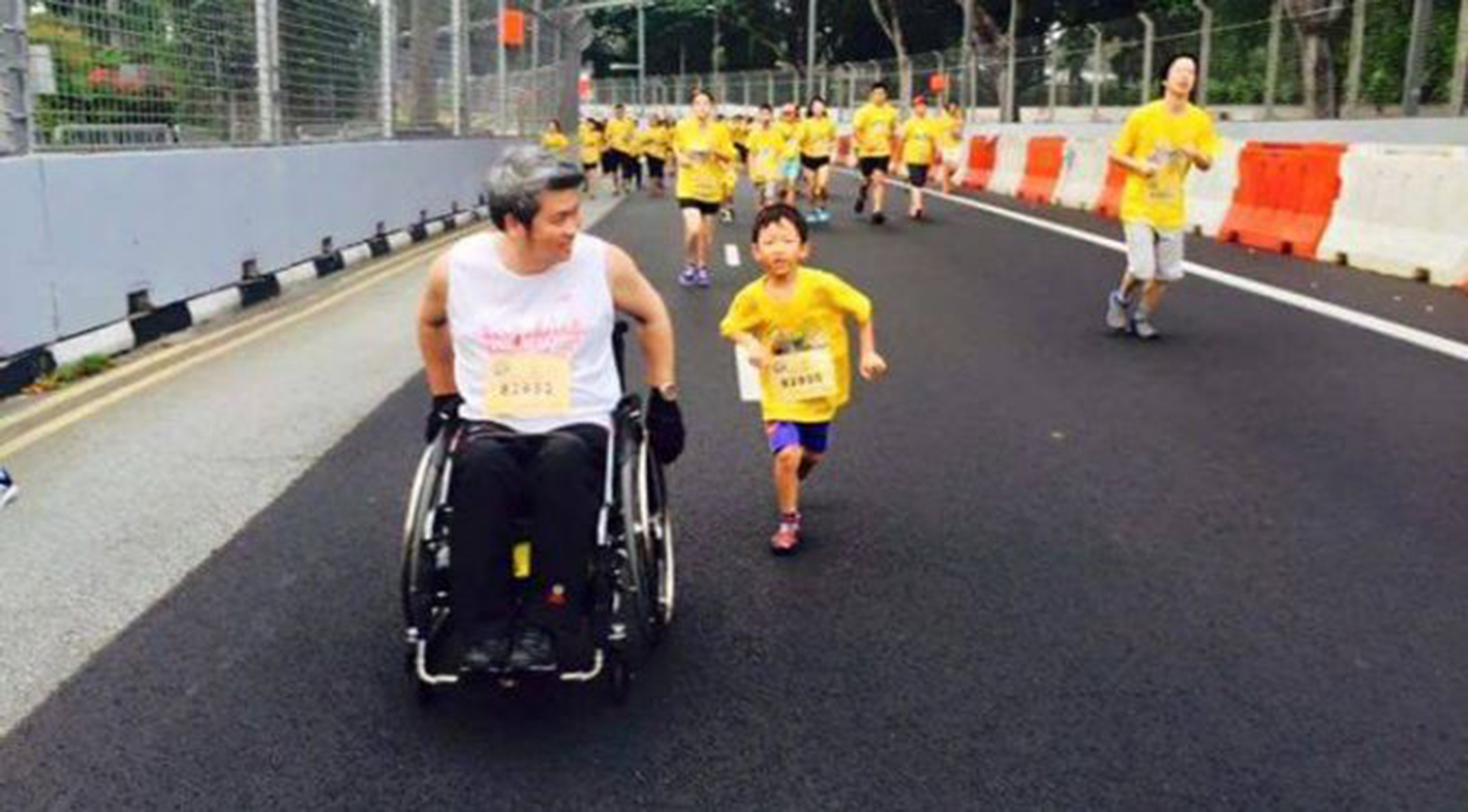 Paraplegic dad wheeling down the street with his son running next to him