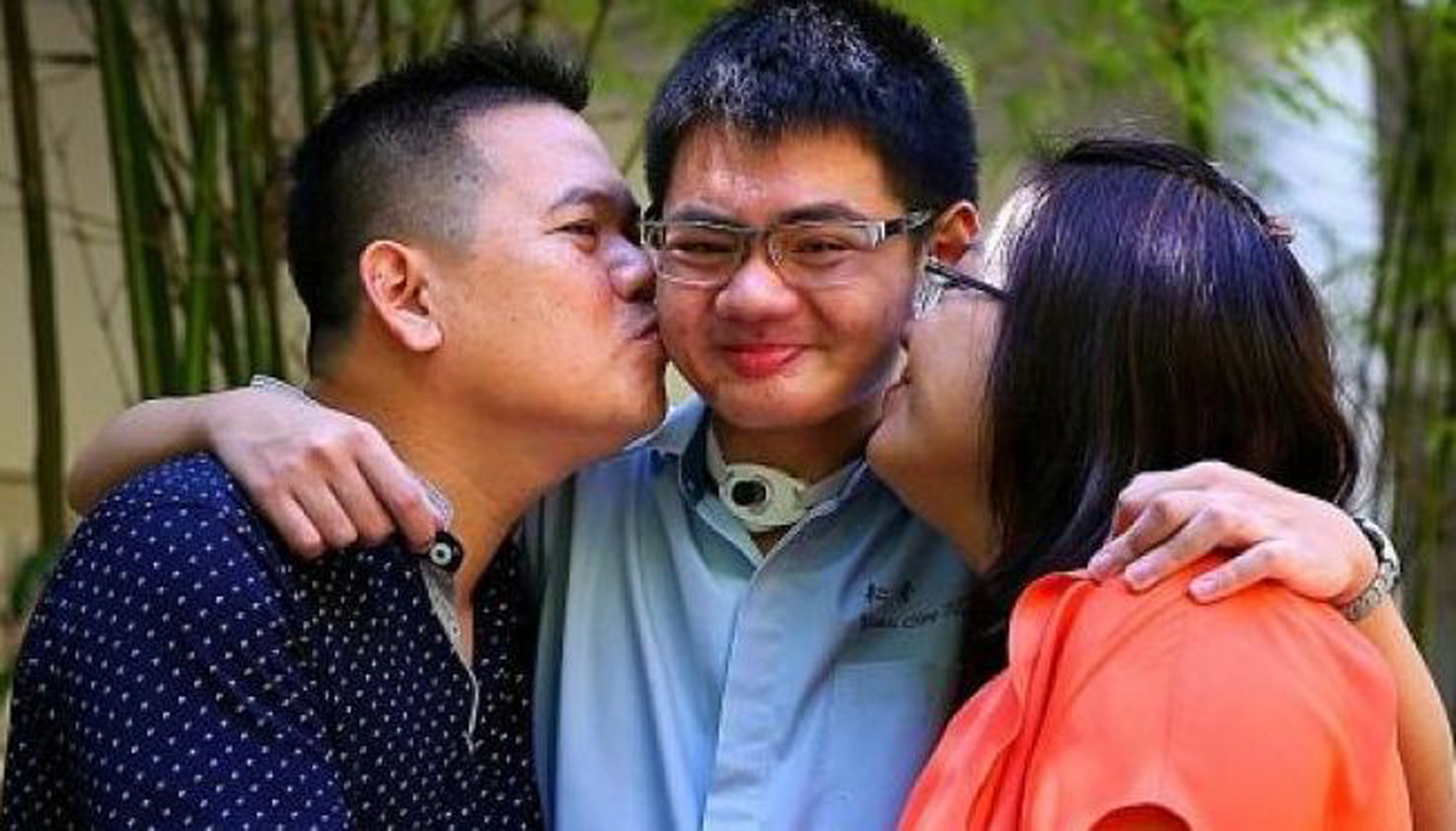 a smiling young man with his parents kissing each of his cheeks