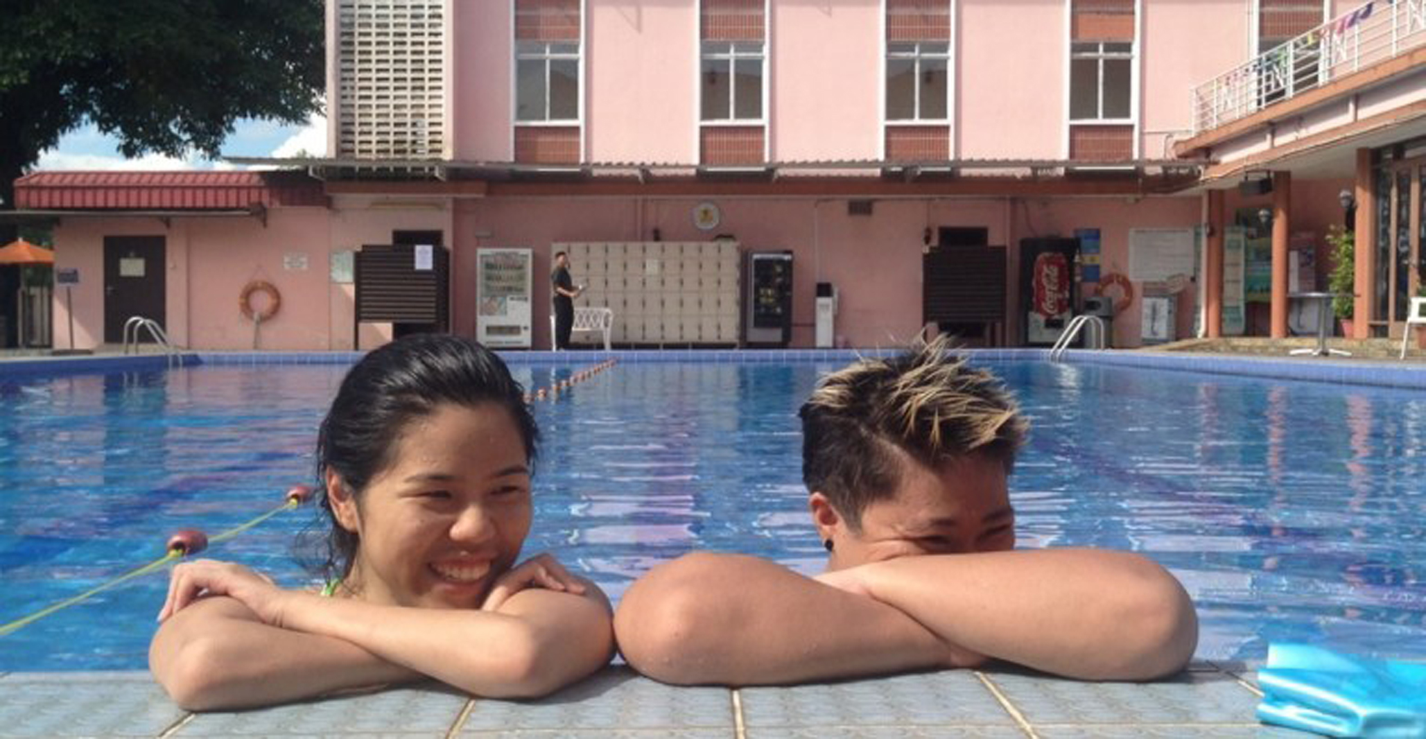 two women in a pool, with their arms crossed over the edge, smiling