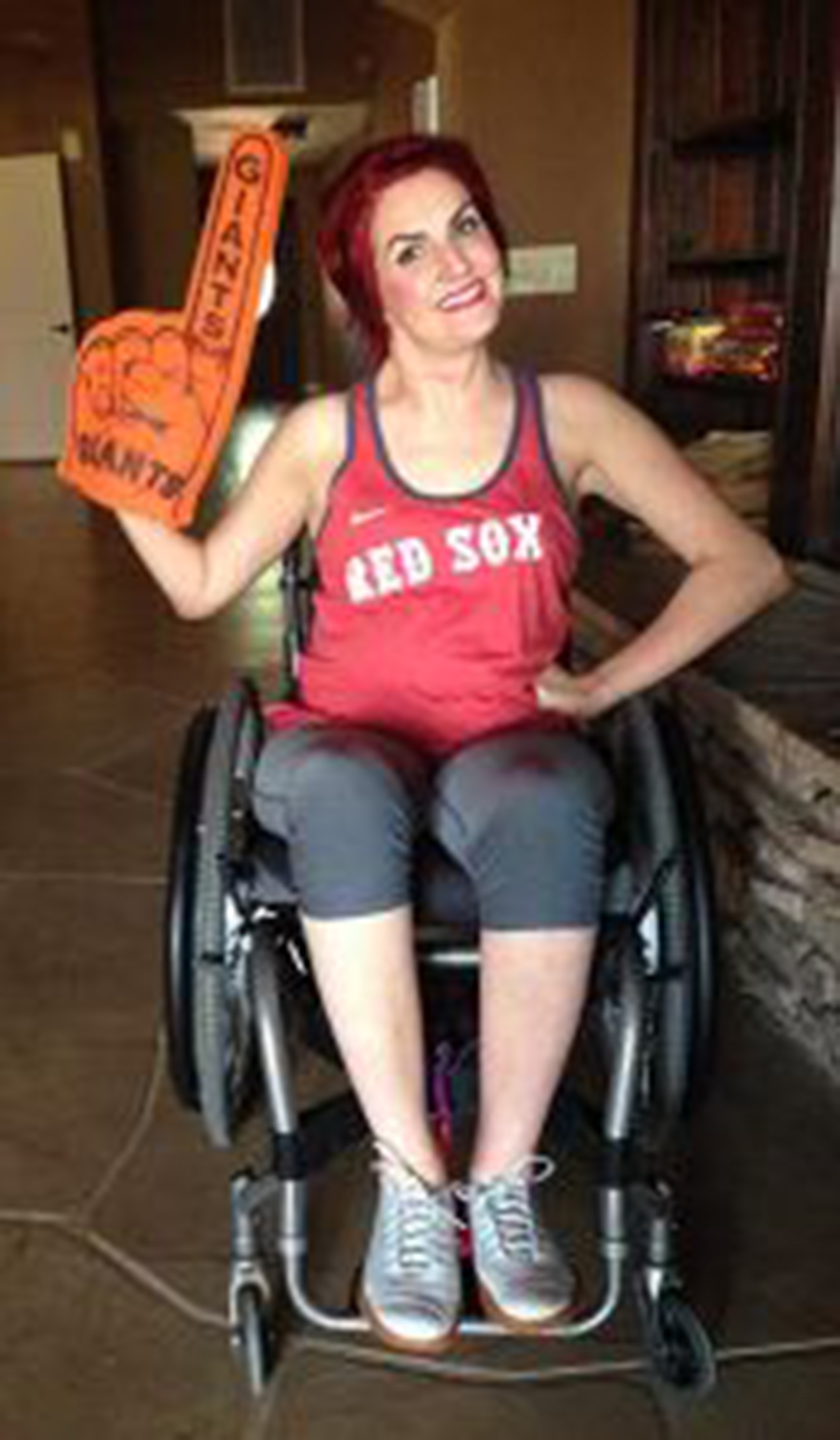 Woman in a manual wheelchair smiling with a foam "number one" hand 