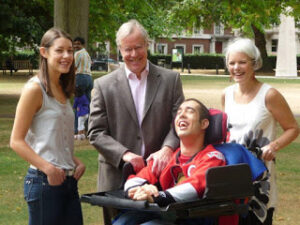 a family of 4 smiling, including one man in a power wheelchair