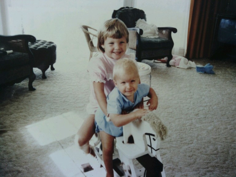 Two young kids riding on a wooden horse