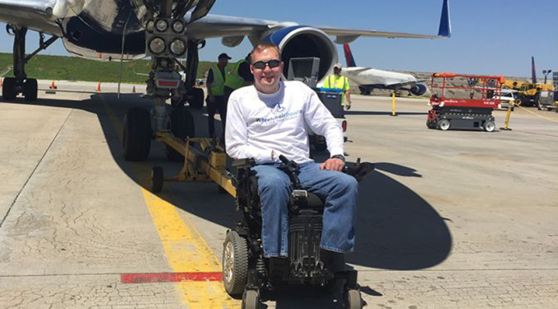 man in power wheelchair in front of an airplane