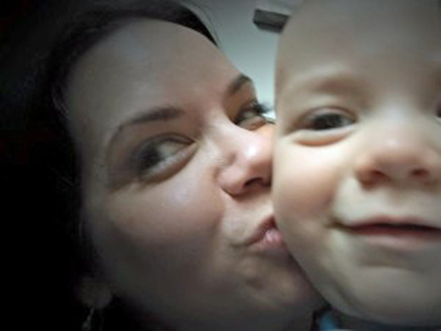 Zoomed in selfie of a mom kissing her toddler son on the cheek
