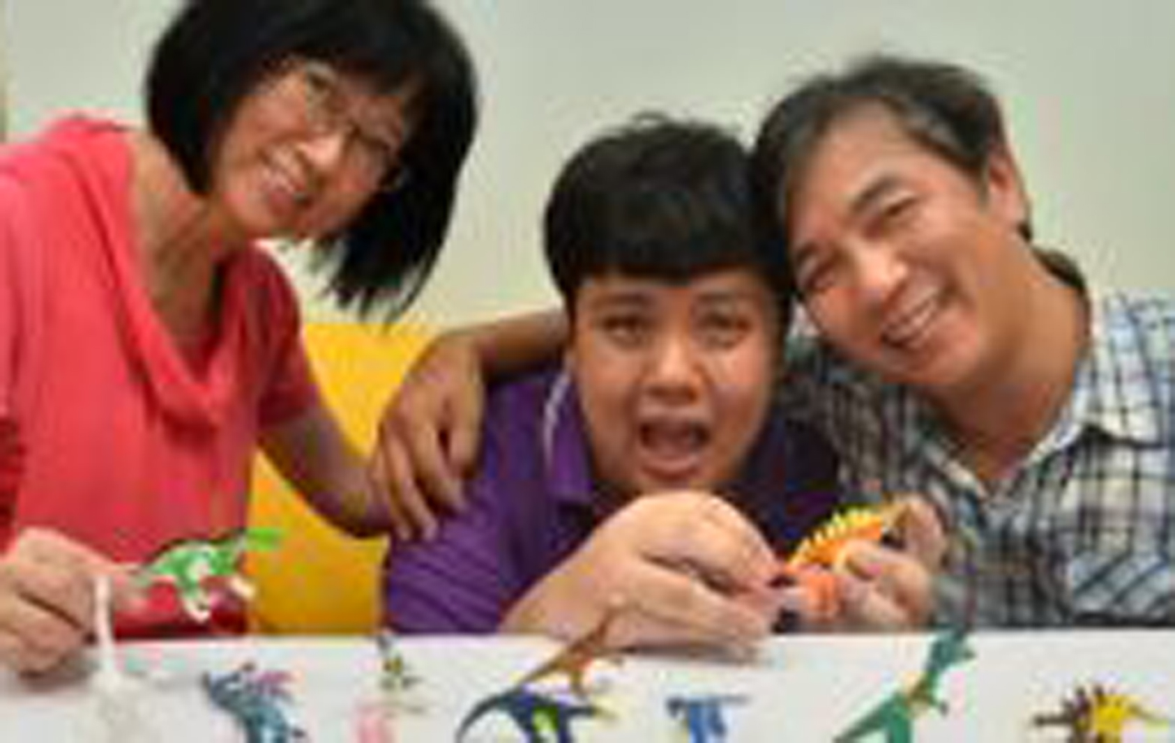 a family of 3 smiling with toy dinosaurs 