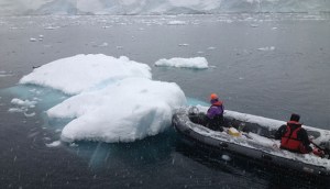 a boat with two people on it next to a small iceberg
