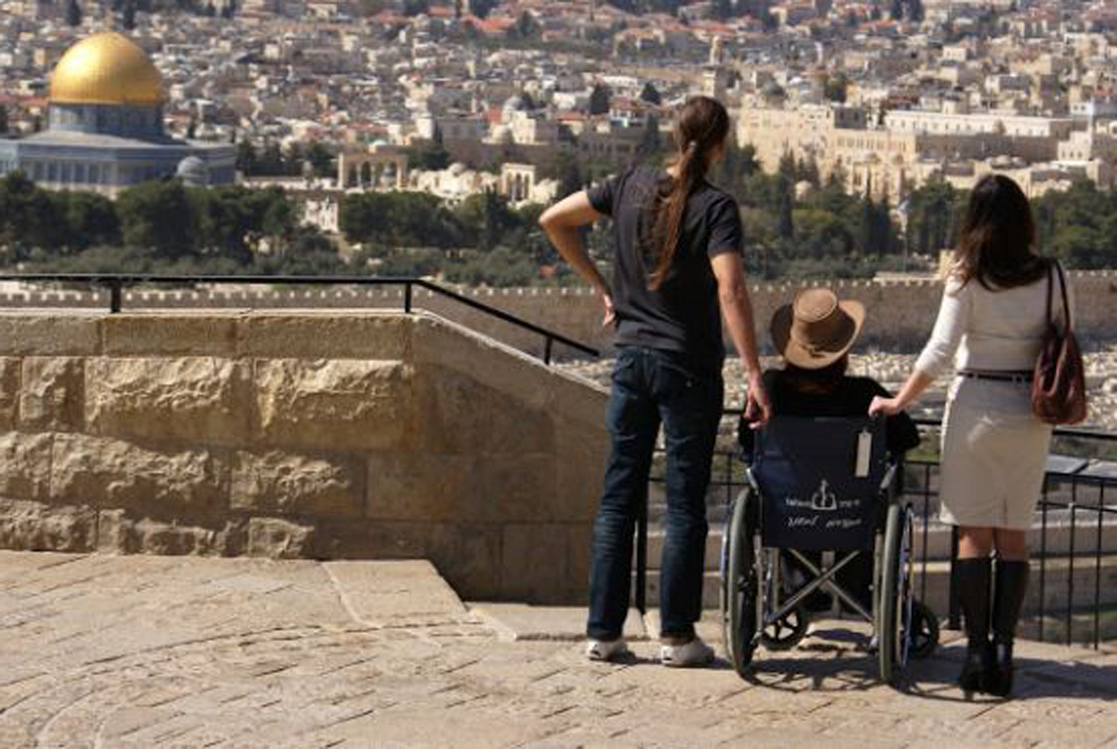 a wheelchair user with two people standing looking down on jerusalem