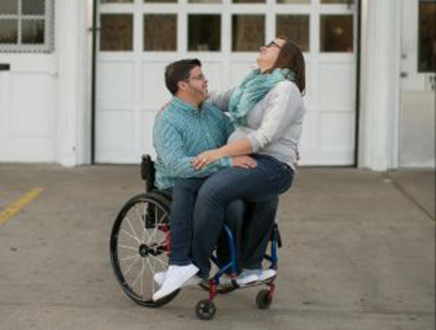 a paraplegic man in a manual chair with his fiancée on his lap laughing