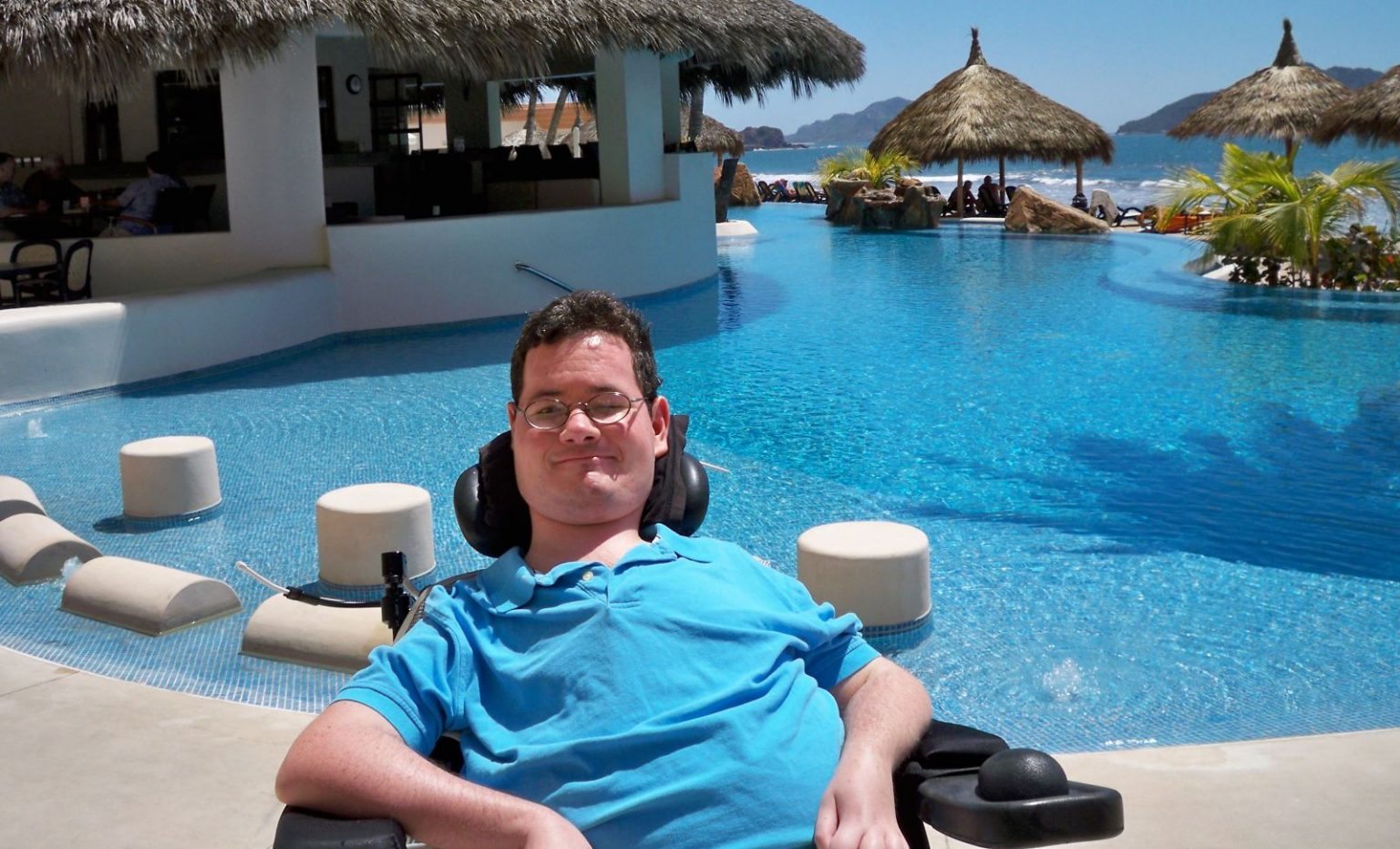 man with muscular dystrophy sits next to a pool