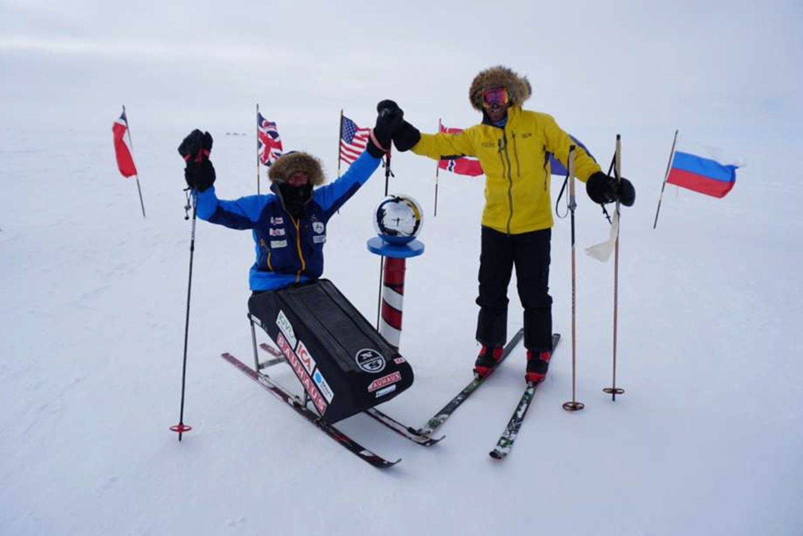 a paraplegic on a sit ski sits next to a man on skis at their south pole expedition