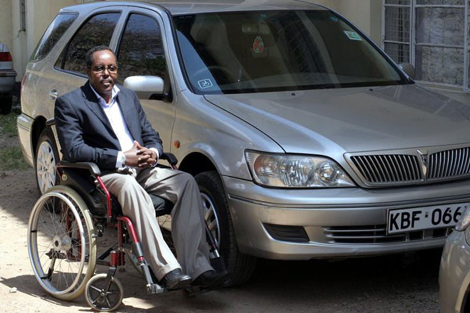 man in a wheelchair sits next to a car
