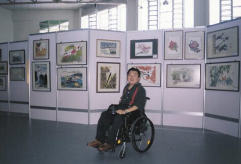 quadriplegic artist sits in front of his paintings