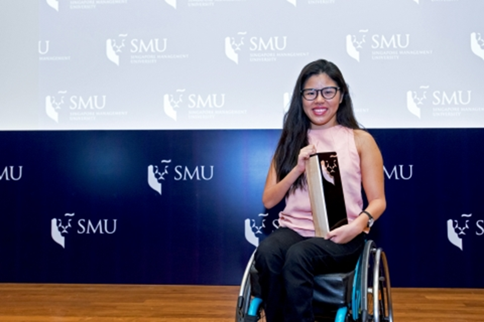 a wheelchair user holds a scholarship trophy