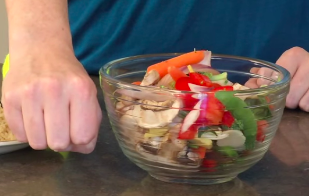 Picture of a hand balled in a fist next to bowl of fruits and vegetables