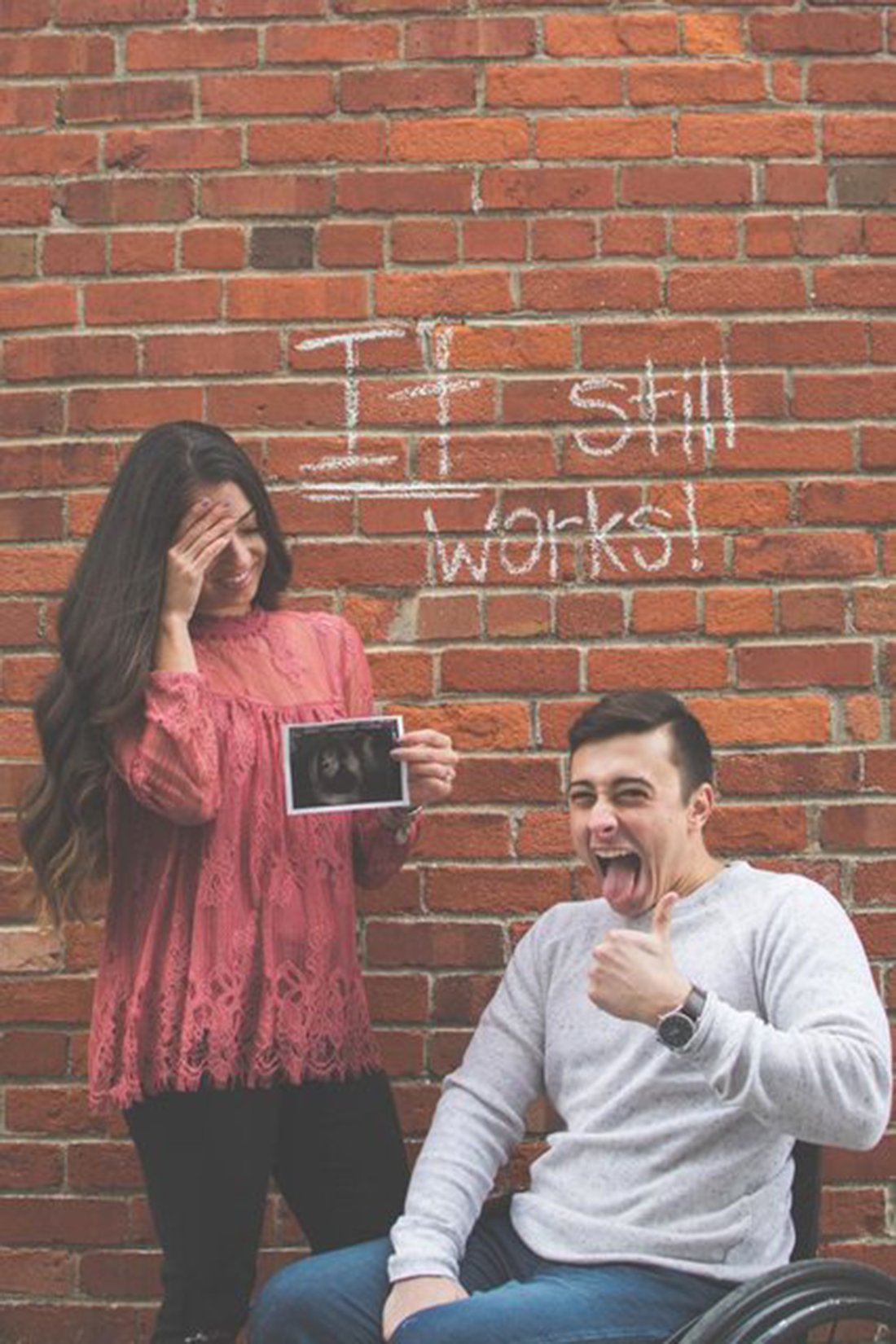 Amanda and todd posing with sonogram in front of brick wall that says it still works