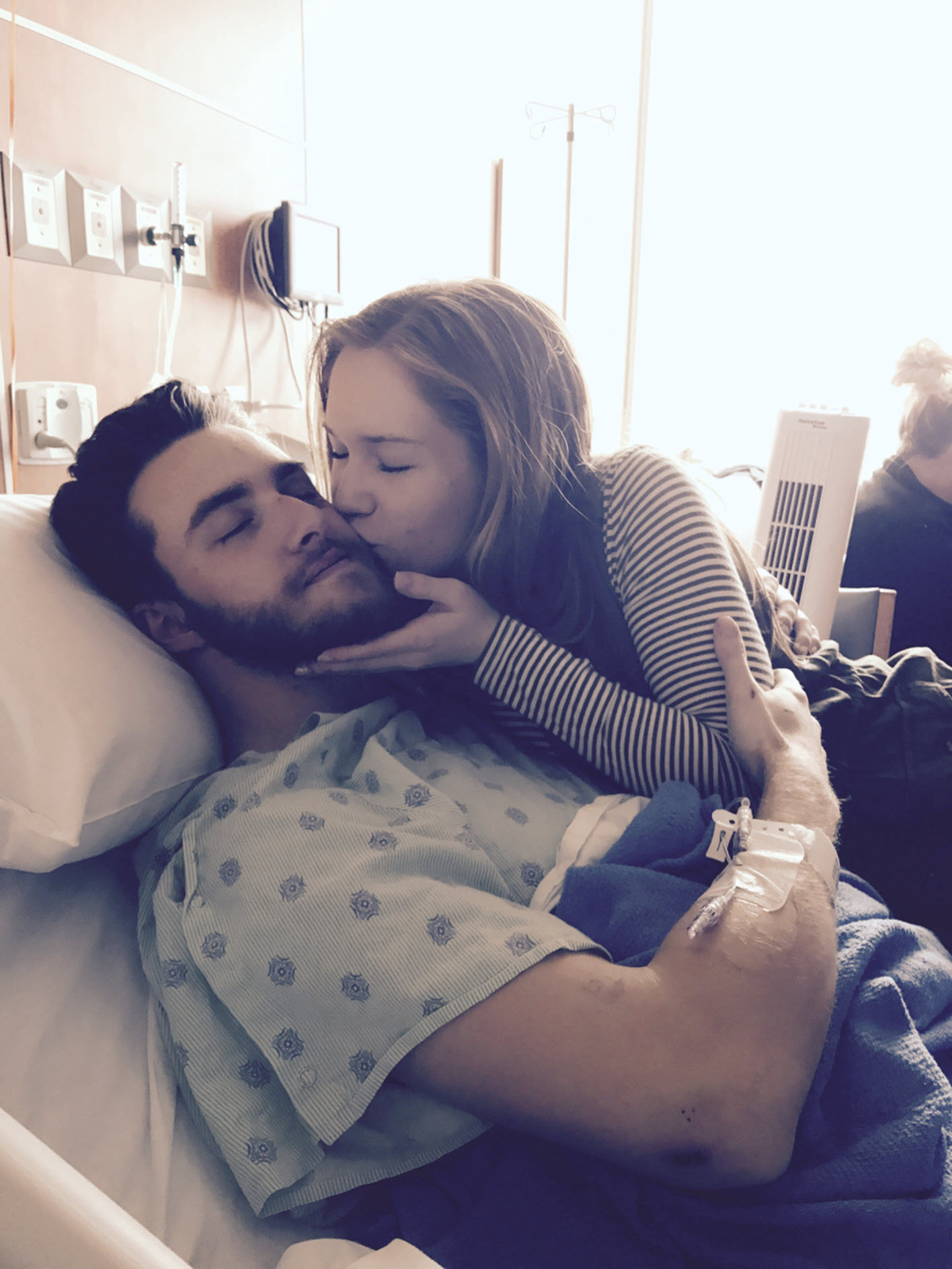 a woman kisses her boyfriend in a hospital bed