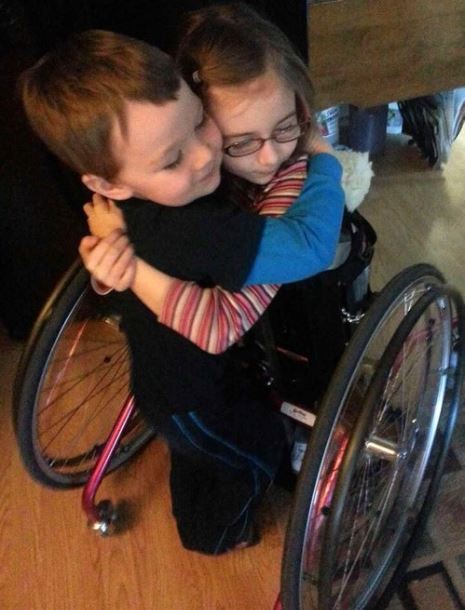Chole and her brother hugging with chole in standing wheelchair