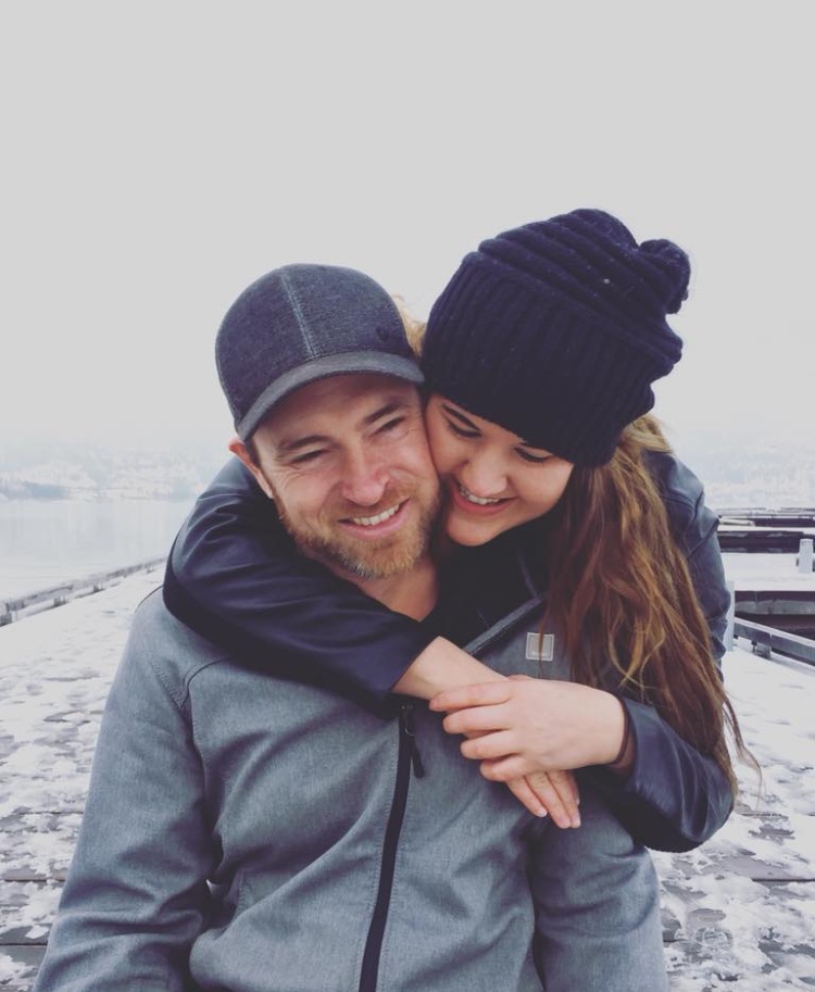 Picture of James and Chelsea. Chelsea is standing behind him with her arms wrapped around his neck.