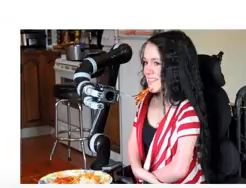 picture of girl in wheelchair using robotic arm to feed herself.