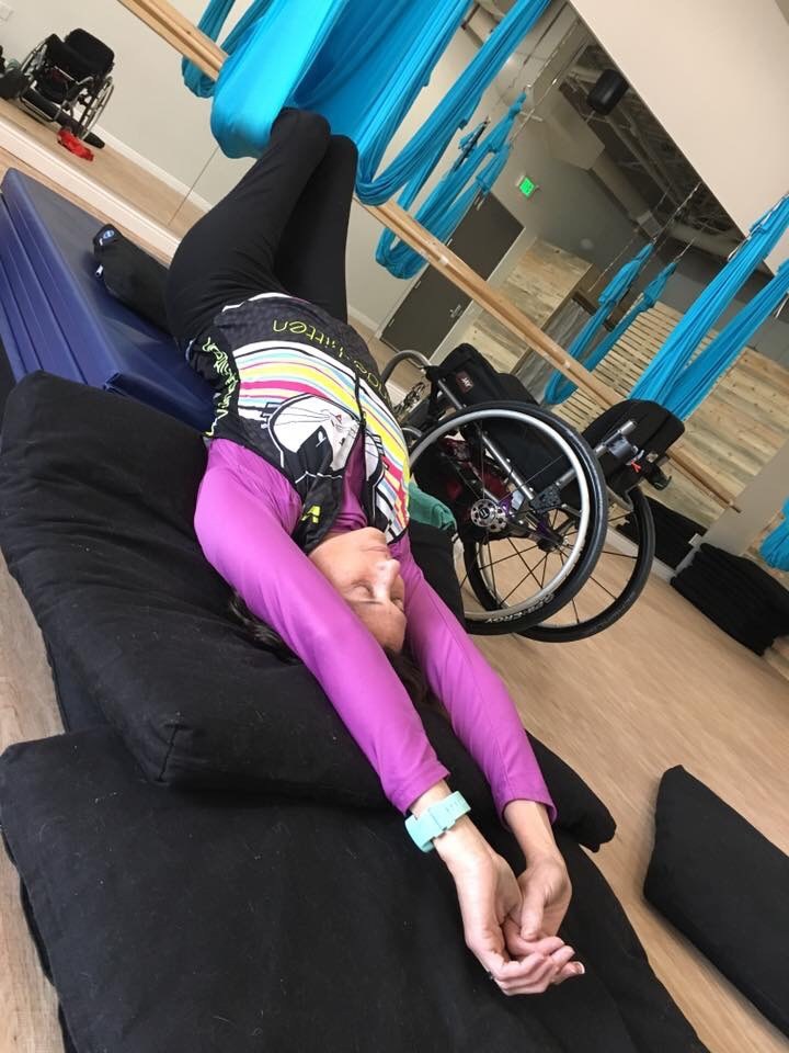 Woman stretching on mat with her legs in silk. Her wheelchair is beside her