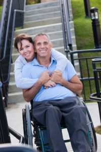Woman hugging man in wheelchair from behind.