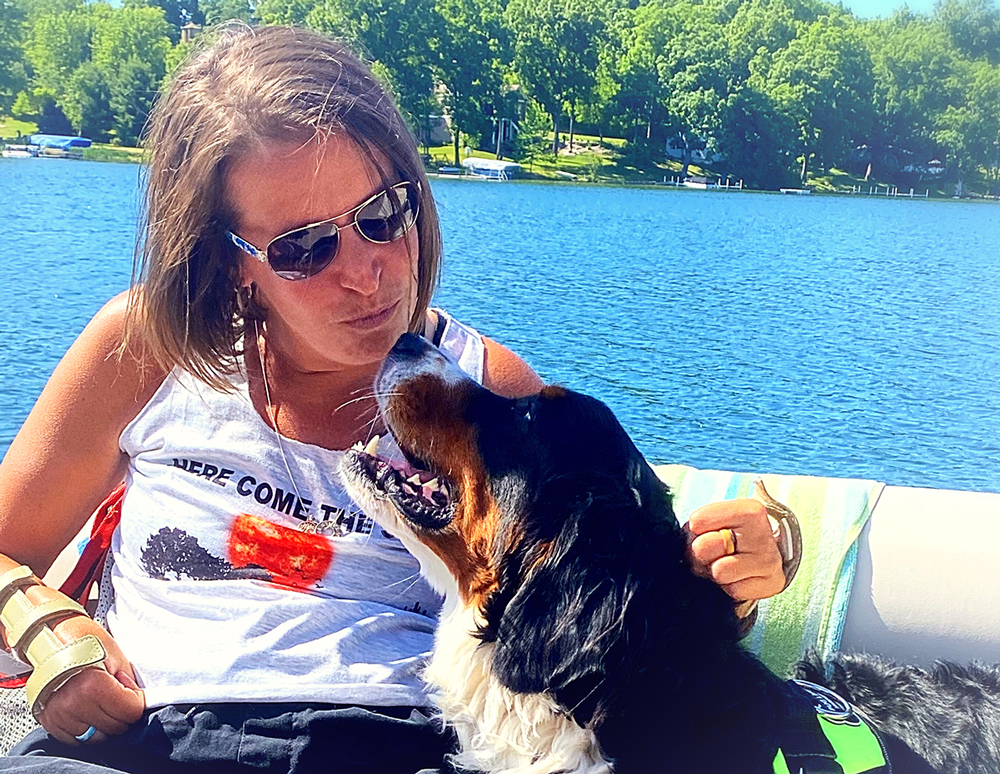 “I’ve been a water girl since birth. We have a lift on our pontoon that allows me to get in my raft and float around or get in our lake.” Annie pictured on the water in pontoon with her dog.