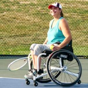 Tenesha on on tennis court with racket and sports wheelchair