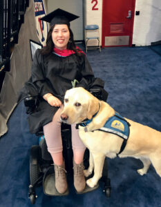 Devins in powerchair wearing graduation cap and gown with yellow lab service dog
