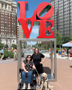 Devins in wheelchair with service dog on leash in front of the Love Statue in Philadelphia