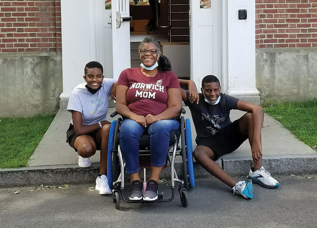 woman sitting in wheelchair bewteen her son and daugher in front of dorm door