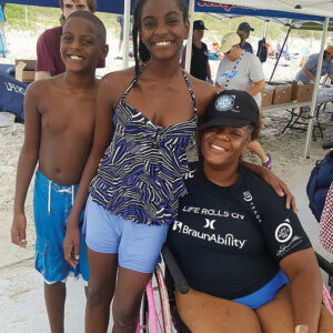 two children standing next to woman in wheelchair in swim suits