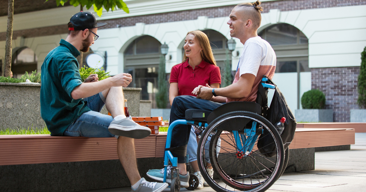 Group of friends taking a stroll on city's street in summer day. Disabled, handicapped man with his friends having fun. Inclusion and diversity concept, normal lifestyle of special groups of society.
