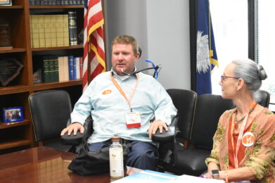 man sitting in powerchair next to woman sitting at conference table 