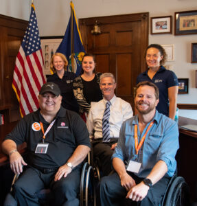 three women standing behind three men in wheelchair in a congressional office