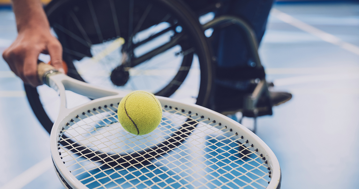 Adult man with a physical disability in a wheelchair playing tennis on indoor tennis court.