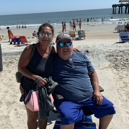 woman standing next to man in powerchair on a crowded beach