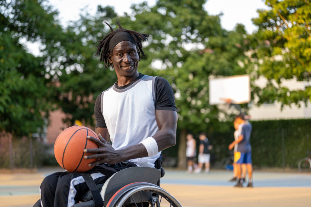 man in wheelchair holding a basketball with net in background