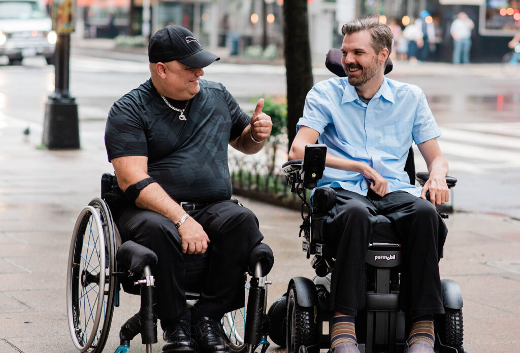 two men in wheelchairs, one is giving a thumbs up