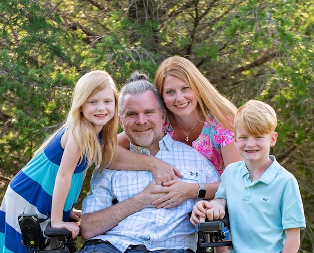 A father using a wheelchair surrounded by his family