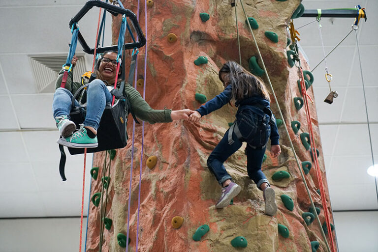 Two young women climb the No Limits adaptive rock wall.