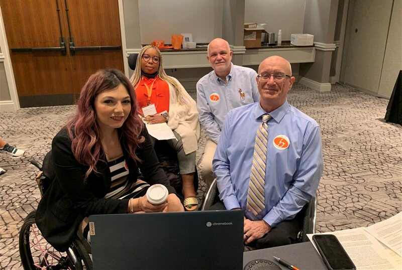 Four wheelchair users in a lobby participating in online meeting via laptop