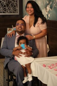 A Black husband and wife are shown with their adorable baby daughter. The husband uses a wheelchair.