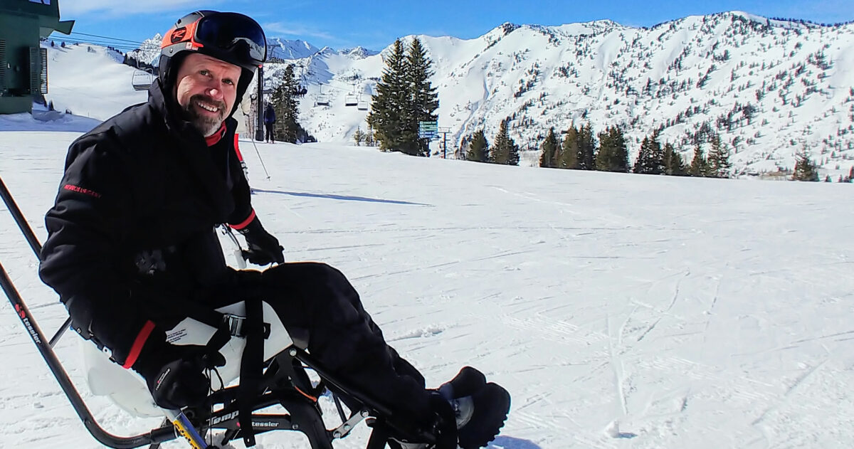 A man sits in a monoski bucket on a ski slope.